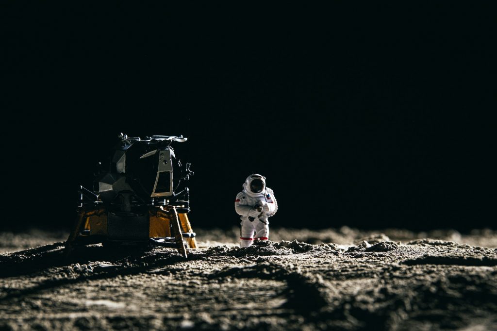 Astronaut miniature toy next to a spaceship on the moon