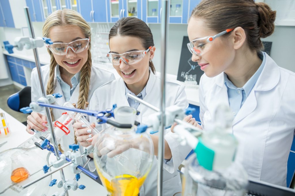 Smiling female scientists in protective eyewear making experiment in chemical laboratory