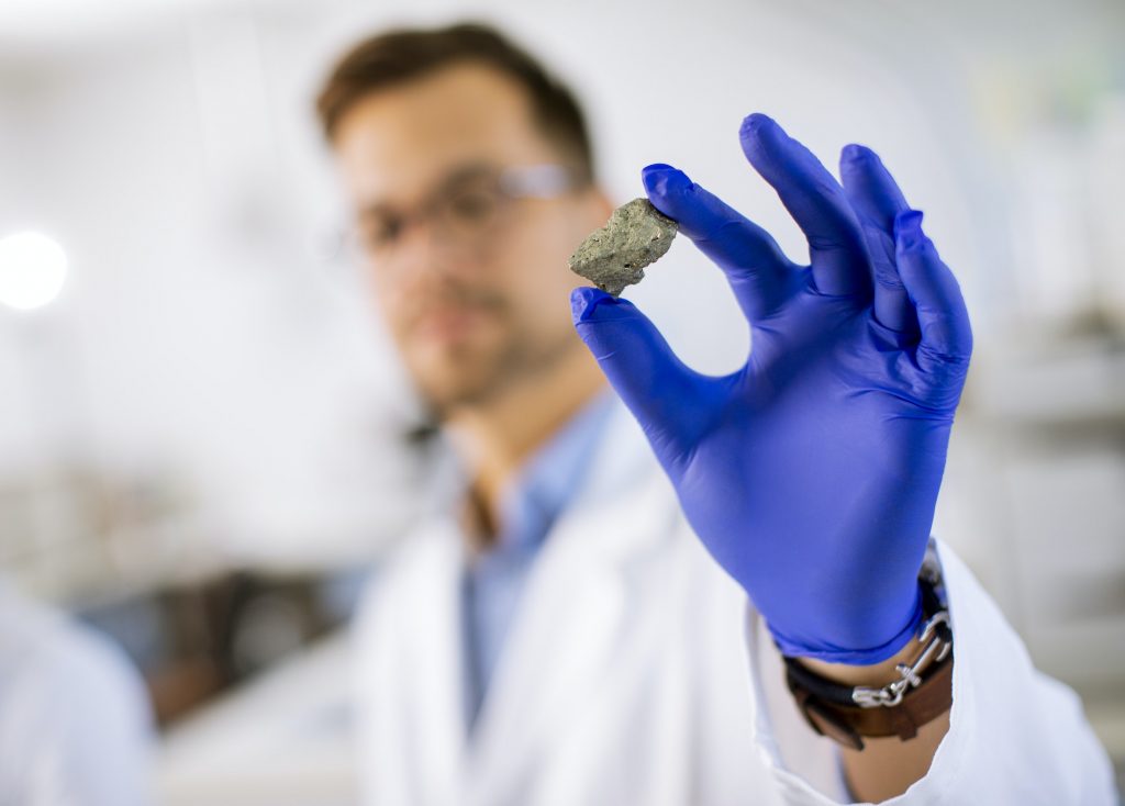 Young scientist hold a mineral specimen in protective glove at material science lab